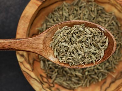 Detailed image of cumin seeds on a wooden spoon for culinary use.