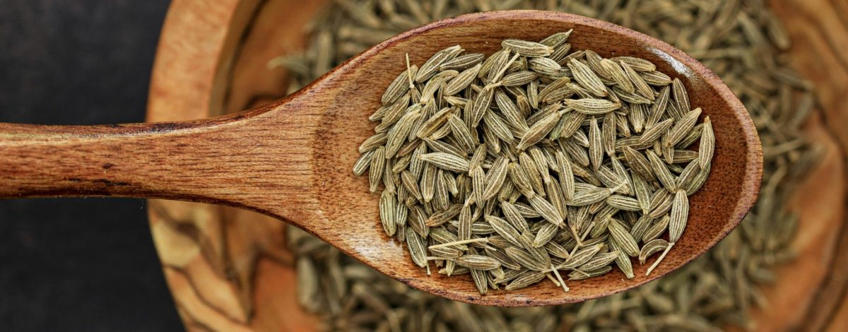 Detailed image of cumin seeds on a wooden spoon for culinary use.