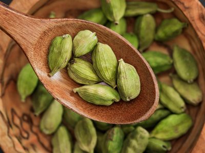 Wooden spoon holding fresh green cardamom on rustic bowl. Ideal for culinary themes.