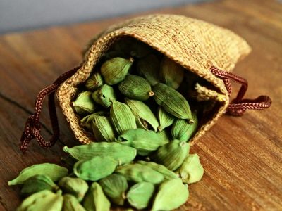 A burlap bag overflowing with fresh green cardamom pods on a rustic wooden table.